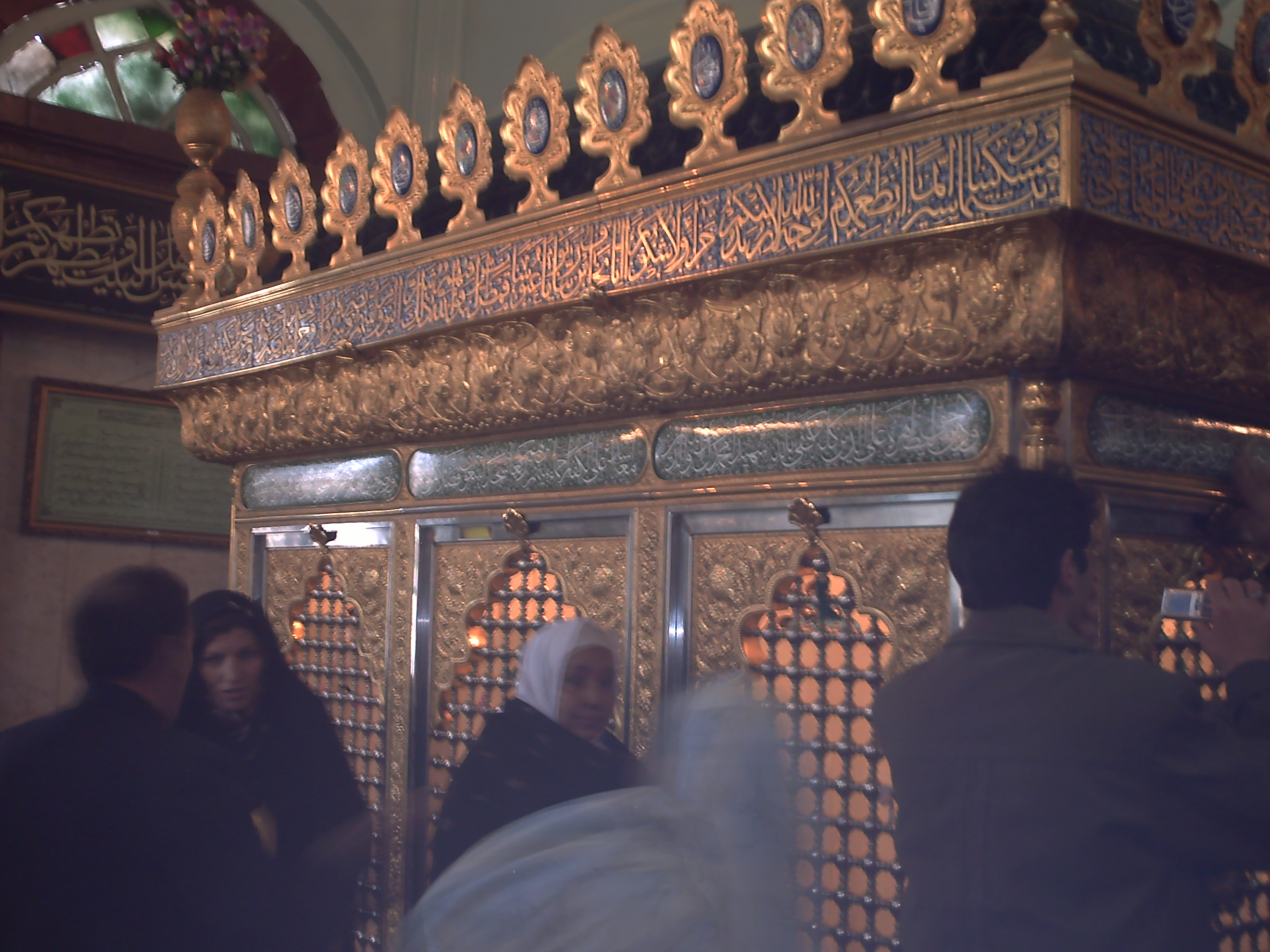 People walk around a fenced gilded indoor enclosure around Sakinah’s tomb